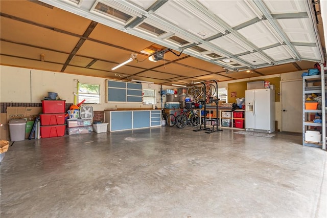 garage with a garage door opener and white refrigerator with ice dispenser