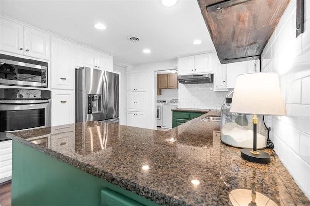 kitchen with tasteful backsplash, separate washer and dryer, dark stone countertops, white cabinets, and appliances with stainless steel finishes