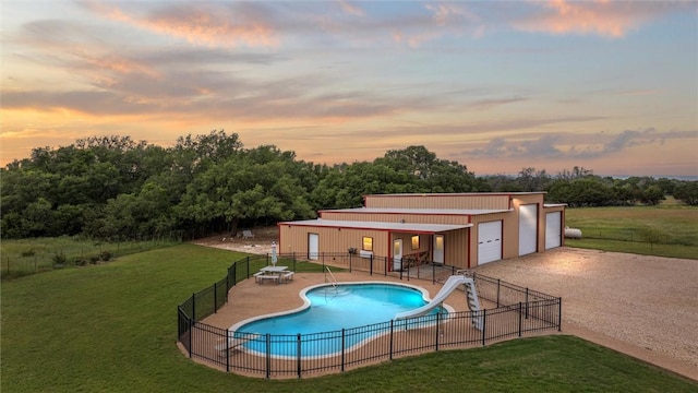 pool at dusk featuring an outbuilding, a yard, a patio, and a water slide