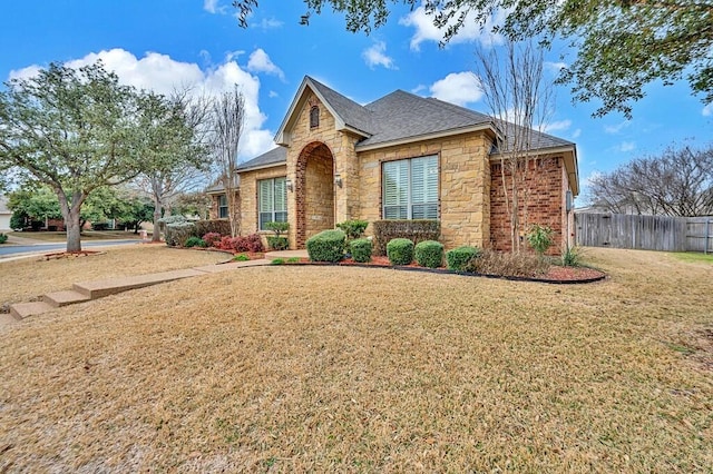 view of front of property featuring stone siding, a front lawn, and fence