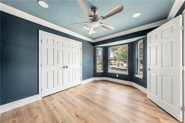 unfurnished bedroom with ornamental molding, light hardwood / wood-style flooring, ceiling fan, and a closet