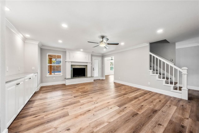 unfurnished living room with crown molding, plenty of natural light, a premium fireplace, and ceiling fan