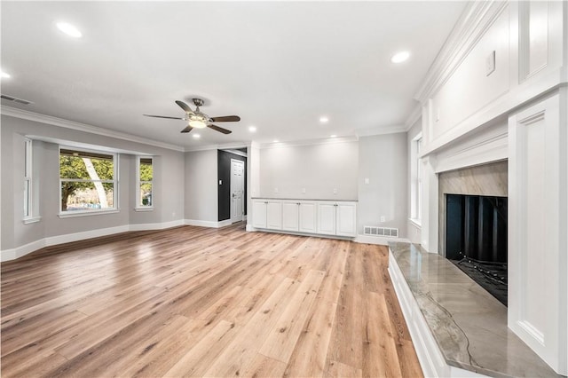 unfurnished living room with crown molding, a high end fireplace, ceiling fan, and light hardwood / wood-style floors