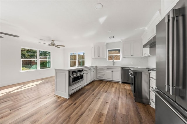 kitchen featuring appliances with stainless steel finishes, sink, white cabinets, decorative backsplash, and wall chimney exhaust hood