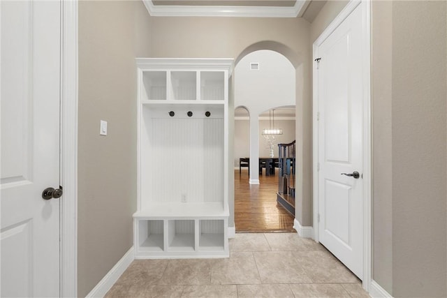 mudroom with crown molding, light tile patterned flooring, and an inviting chandelier