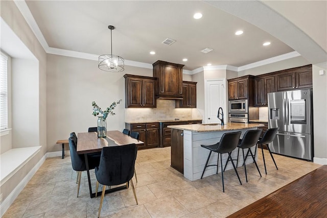 kitchen featuring hanging light fixtures, a kitchen island with sink, dark brown cabinetry, stainless steel appliances, and light stone countertops