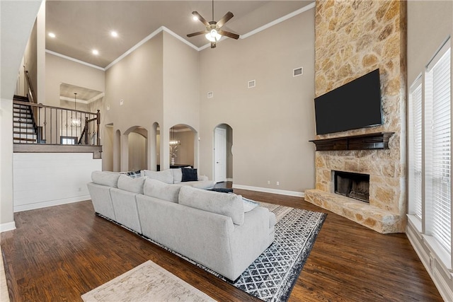 living room featuring a stone fireplace, dark hardwood / wood-style floors, ornamental molding, ceiling fan, and a healthy amount of sunlight