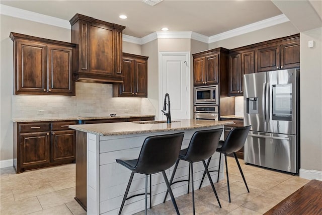 kitchen with a kitchen island with sink, sink, stainless steel appliances, and dark brown cabinetry