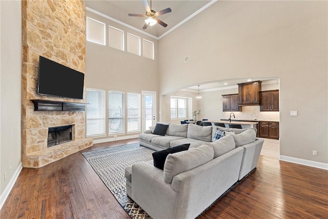 living room with a stone fireplace, dark hardwood / wood-style floors, sink, ceiling fan, and crown molding