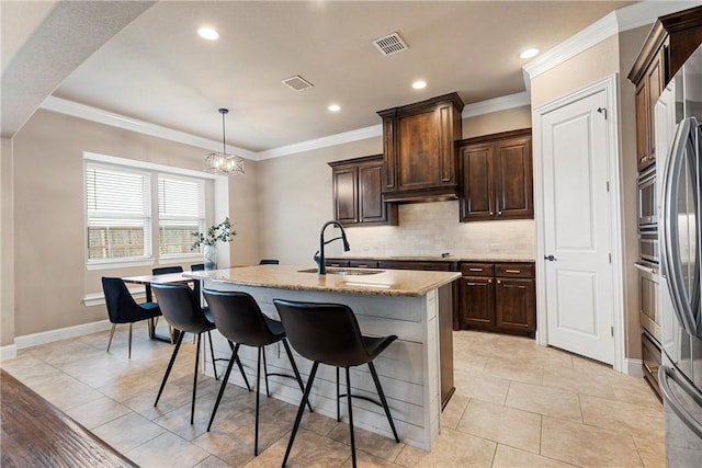 kitchen with sink, light stone counters, decorative light fixtures, a center island with sink, and decorative backsplash