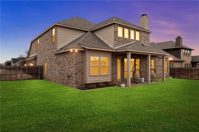 back house at dusk with a patio and a lawn