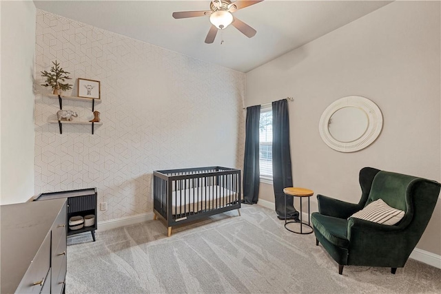 bedroom with a nursery area, light colored carpet, and ceiling fan