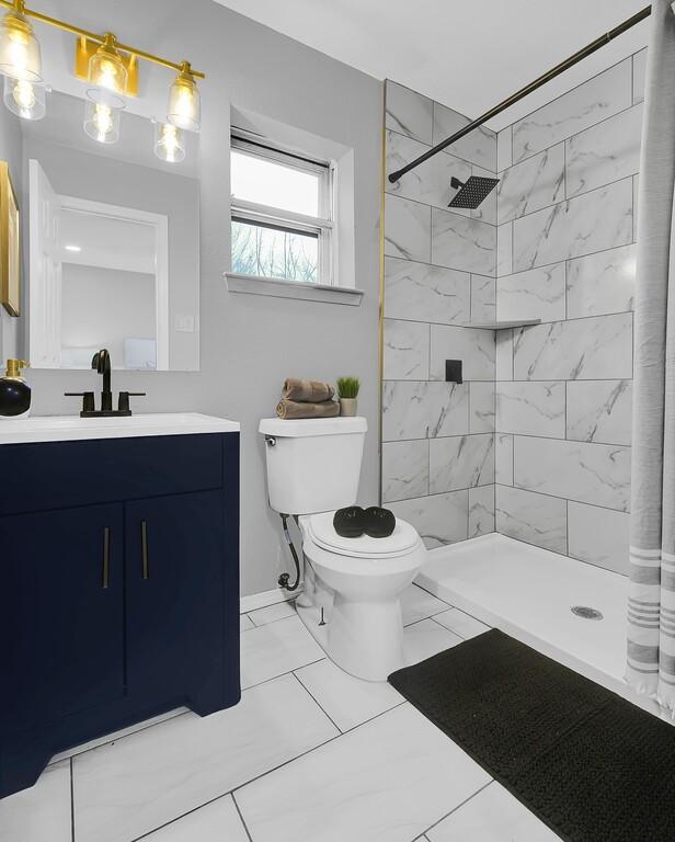 bathroom with tiled shower, vanity, and toilet