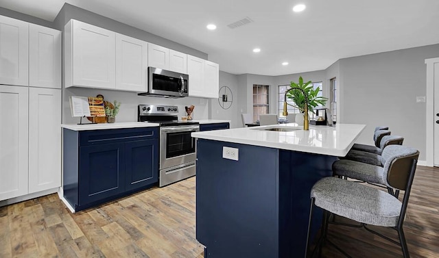 kitchen featuring light hardwood / wood-style flooring, a breakfast bar, appliances with stainless steel finishes, an island with sink, and white cabinets