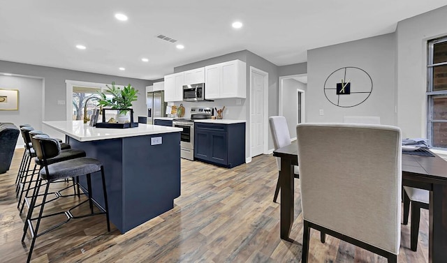 kitchen featuring white cabinetry, a kitchen bar, a kitchen island with sink, stainless steel appliances, and blue cabinetry