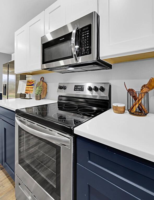 kitchen with stainless steel appliances, blue cabinetry, white cabinets, and light hardwood / wood-style flooring