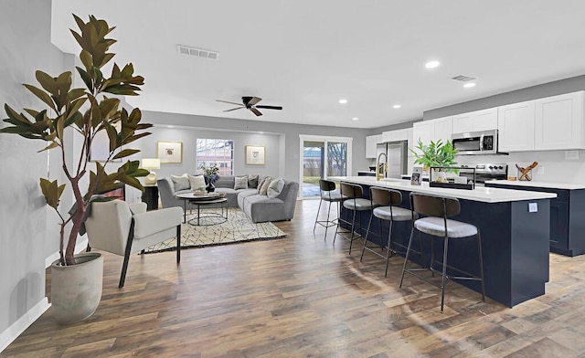 kitchen featuring appliances with stainless steel finishes, white cabinetry, a kitchen breakfast bar, dark hardwood / wood-style floors, and a center island with sink