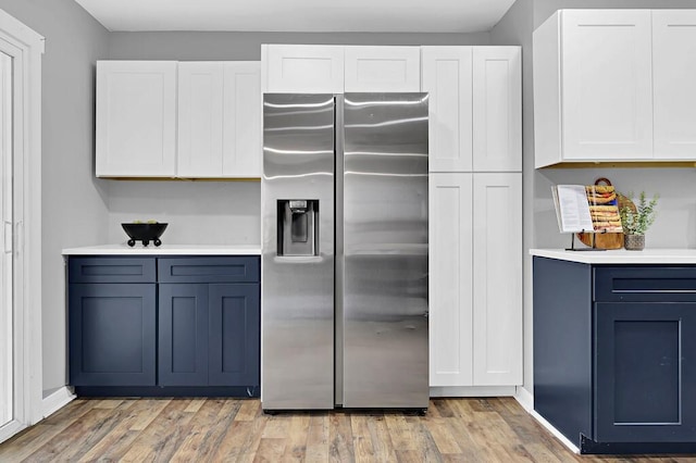 kitchen with blue cabinetry, stainless steel fridge, light wood-type flooring, and white cabinets