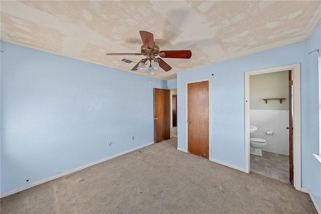 unfurnished bedroom featuring ceiling fan, ensuite bathroom, light carpet, and tile walls