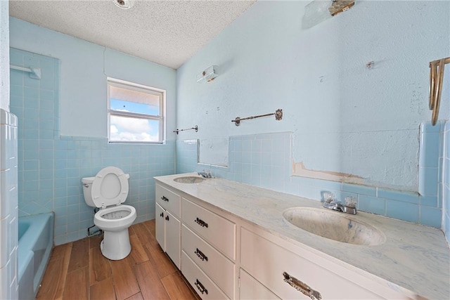 bathroom with wood-type flooring, a textured ceiling, toilet, vanity, and tile walls