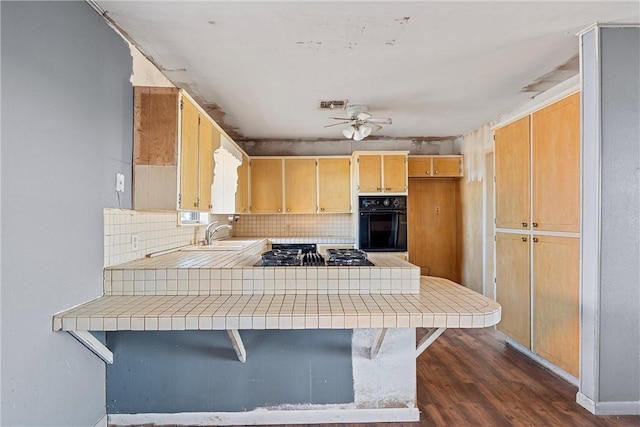 kitchen with black appliances, a kitchen breakfast bar, kitchen peninsula, and tile counters