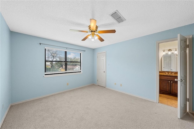 unfurnished bedroom with a textured ceiling, light colored carpet, ceiling fan, and ensuite bathroom