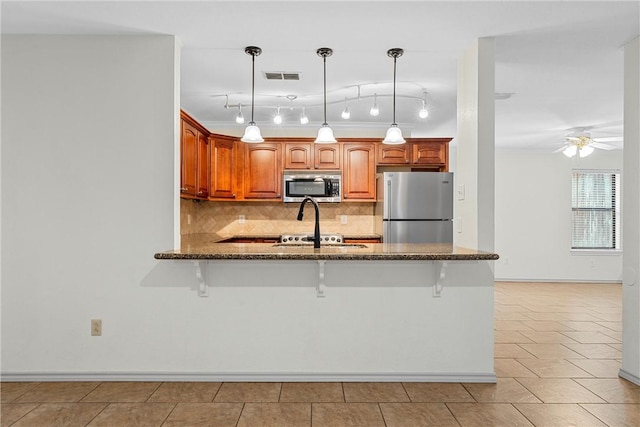 kitchen with ceiling fan, a kitchen bar, appliances with stainless steel finishes, and tasteful backsplash