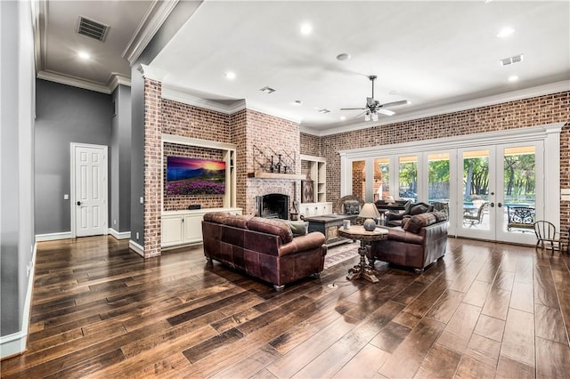 living room with french doors, crown molding, a brick fireplace, ceiling fan, and brick wall