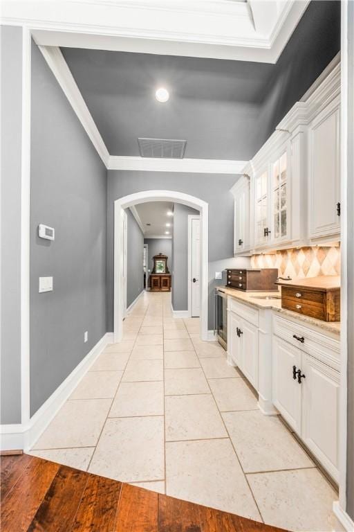 kitchen with wine cooler, white cabinets, light tile patterned floors, and ornamental molding