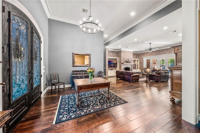 foyer with french doors, dark hardwood / wood-style flooring, ceiling fan with notable chandelier, crown molding, and a fireplace