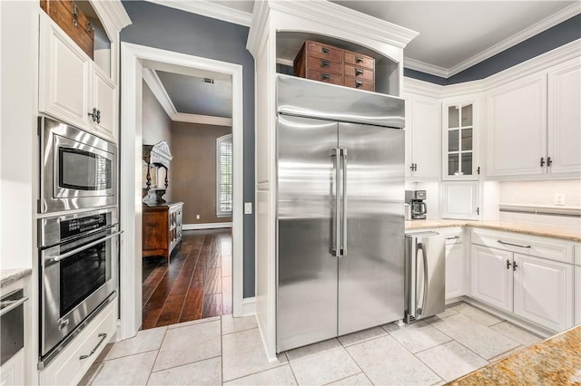 kitchen with built in appliances, white cabinetry, and crown molding