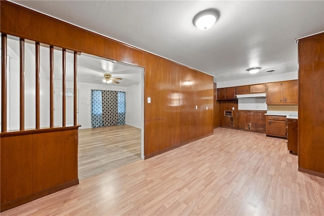 unfurnished living room with ceiling fan, light hardwood / wood-style flooring, and wooden walls