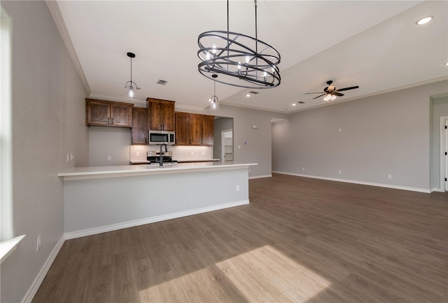 kitchen with appliances with stainless steel finishes, dark hardwood / wood-style flooring, ceiling fan with notable chandelier, crown molding, and pendant lighting