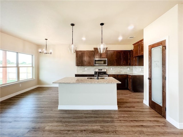 kitchen with backsplash, light stone counters, dark wood-type flooring, hanging light fixtures, and an island with sink