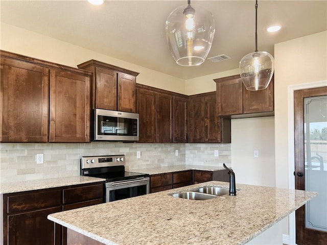 kitchen with light stone counters, sink, pendant lighting, and appliances with stainless steel finishes