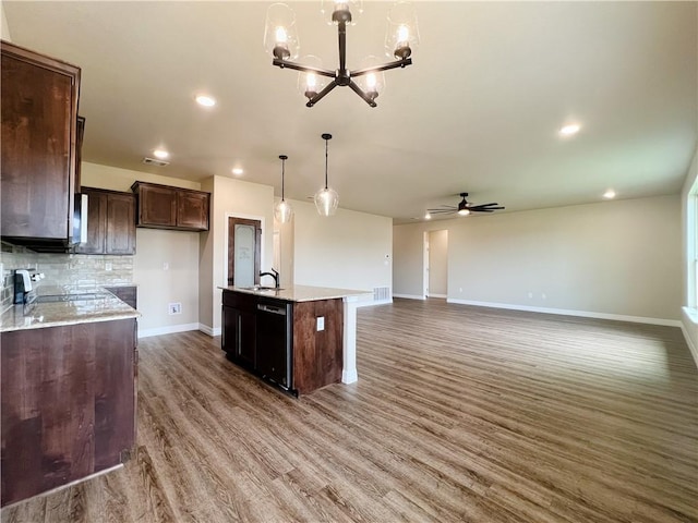 kitchen with pendant lighting, backsplash, ceiling fan with notable chandelier, sink, and an island with sink