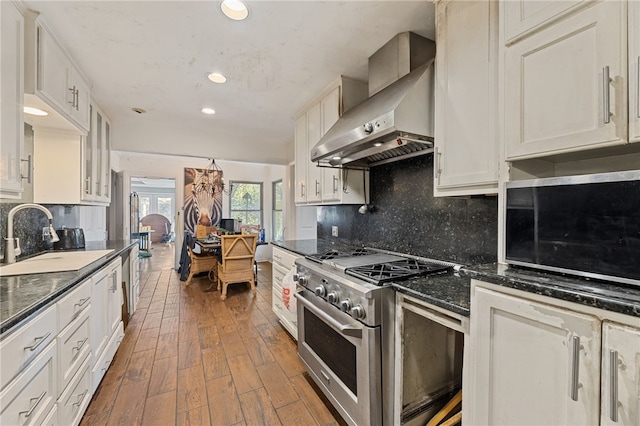 kitchen featuring sink, wall chimney exhaust hood, dark wood-type flooring, high end stainless steel range, and white cabinets