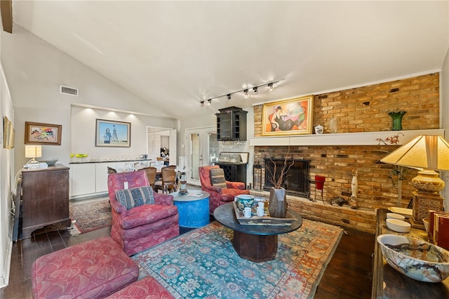 living room with dark wood-type flooring, brick wall, track lighting, vaulted ceiling, and a fireplace