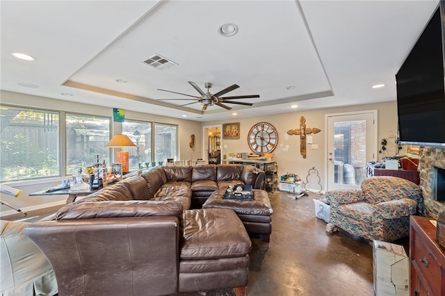 living room with a raised ceiling, ceiling fan, and a fireplace