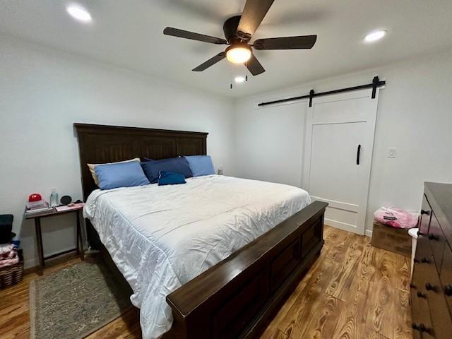 bedroom with hardwood / wood-style flooring, a barn door, and ceiling fan