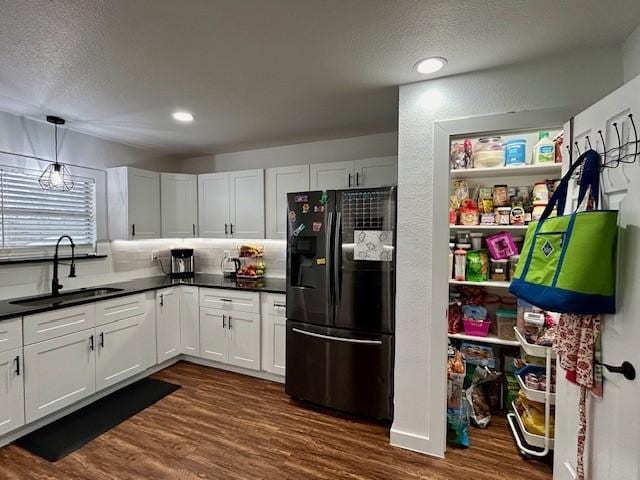 kitchen with dark wood-type flooring, sink, black refrigerator, pendant lighting, and white cabinets