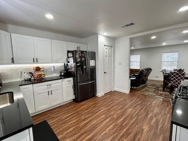 kitchen with black refrigerator, dark wood-type flooring, tasteful backsplash, and white cabinets