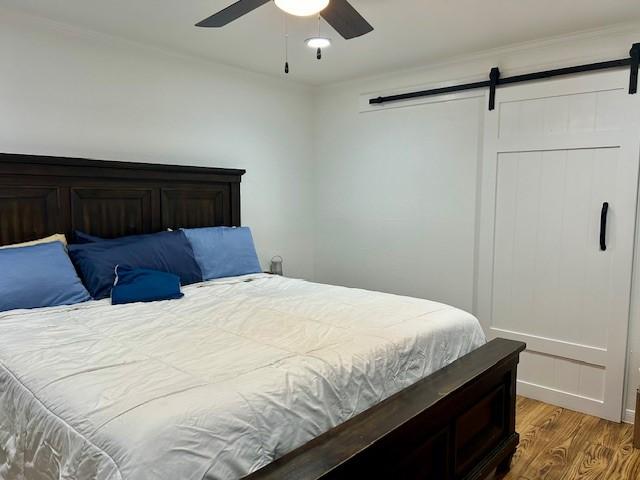 bedroom with wood-type flooring, a barn door, and ceiling fan