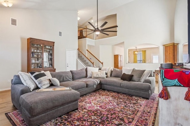 living area featuring arched walkways, ceiling fan, visible vents, stairway, and light wood-type flooring