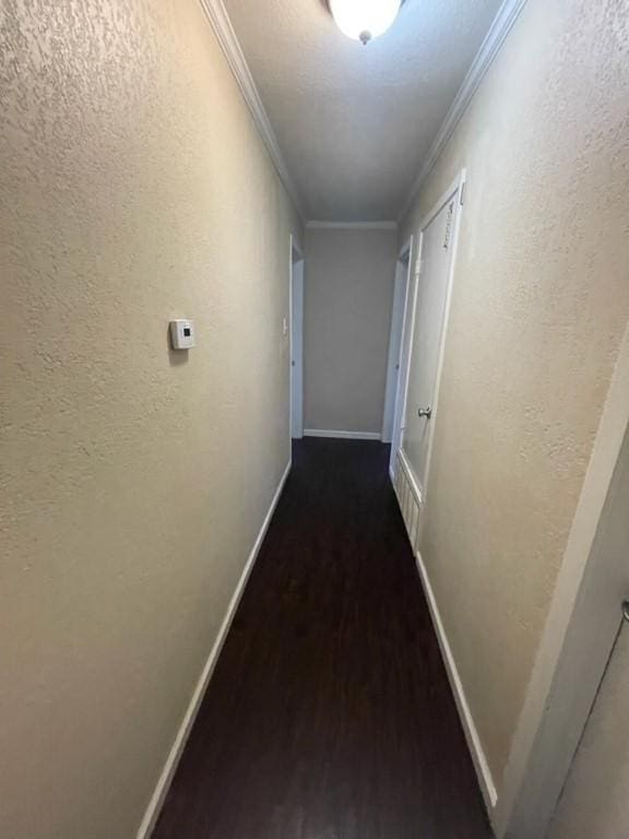 hall featuring a textured wall, crown molding, baseboards, and wood finished floors