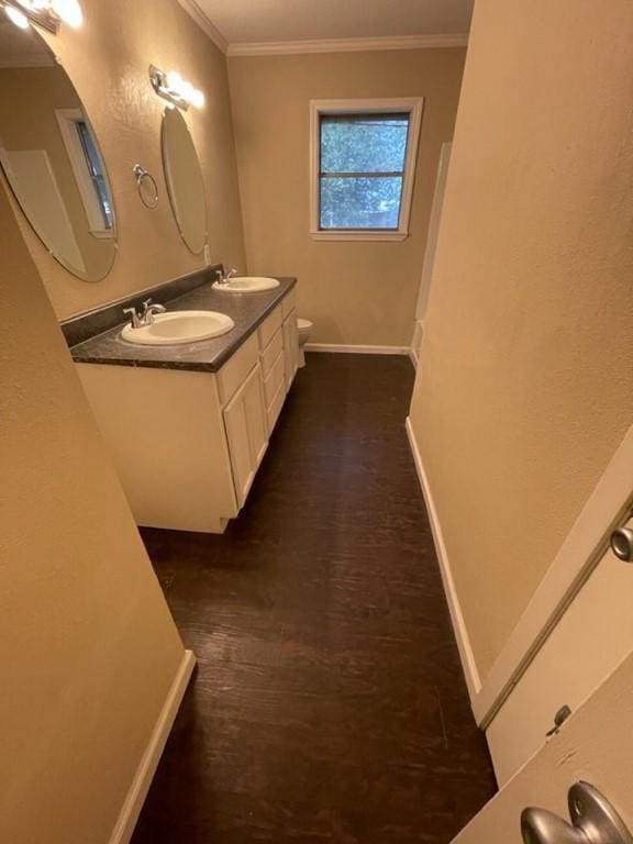 bathroom featuring crown molding, baseboards, a sink, and wood finished floors