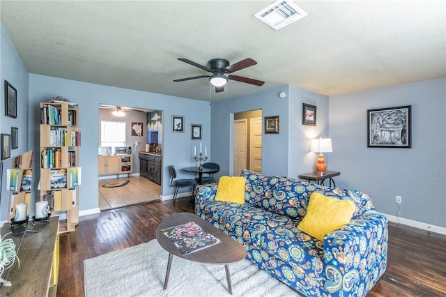 living room with dark wood-type flooring, ceiling fan, and a textured ceiling