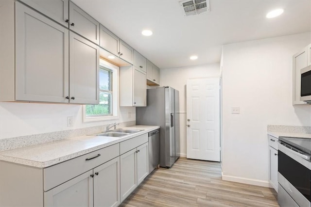 kitchen featuring appliances with stainless steel finishes, light wood-type flooring, gray cabinetry, and sink