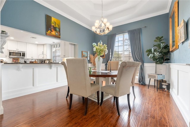 dining area with wainscoting, an inviting chandelier, wood finished floors, a decorative wall, and a raised ceiling