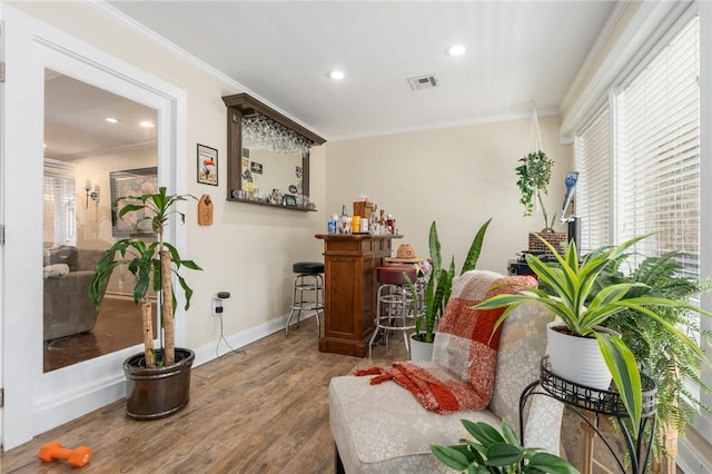 living area featuring visible vents, crown molding, baseboards, wood finished floors, and a bar